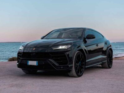 Lamborghini Urus in sleek black parked by the Ibiza shoreline, ready for rent